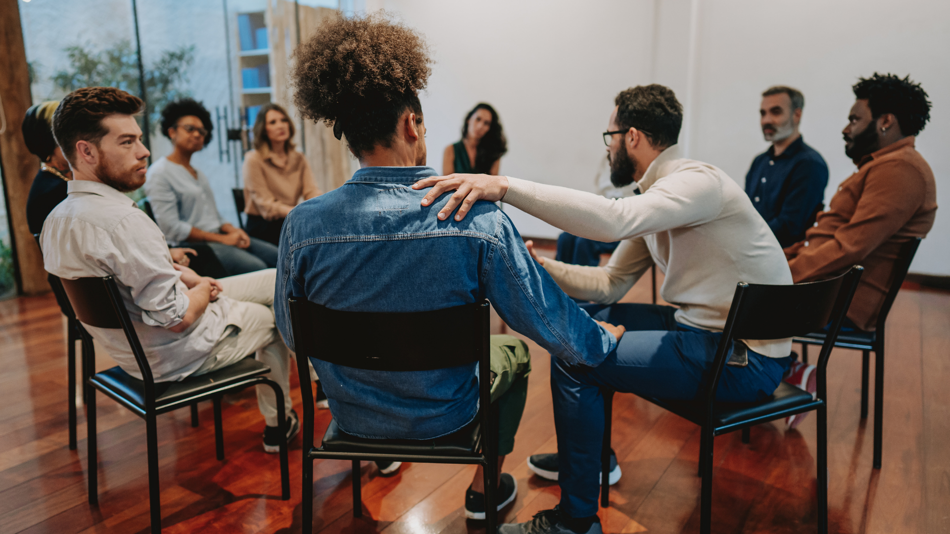 People seated in a circle in a discussion group, with one person gesturing during a meeting in a bright room.