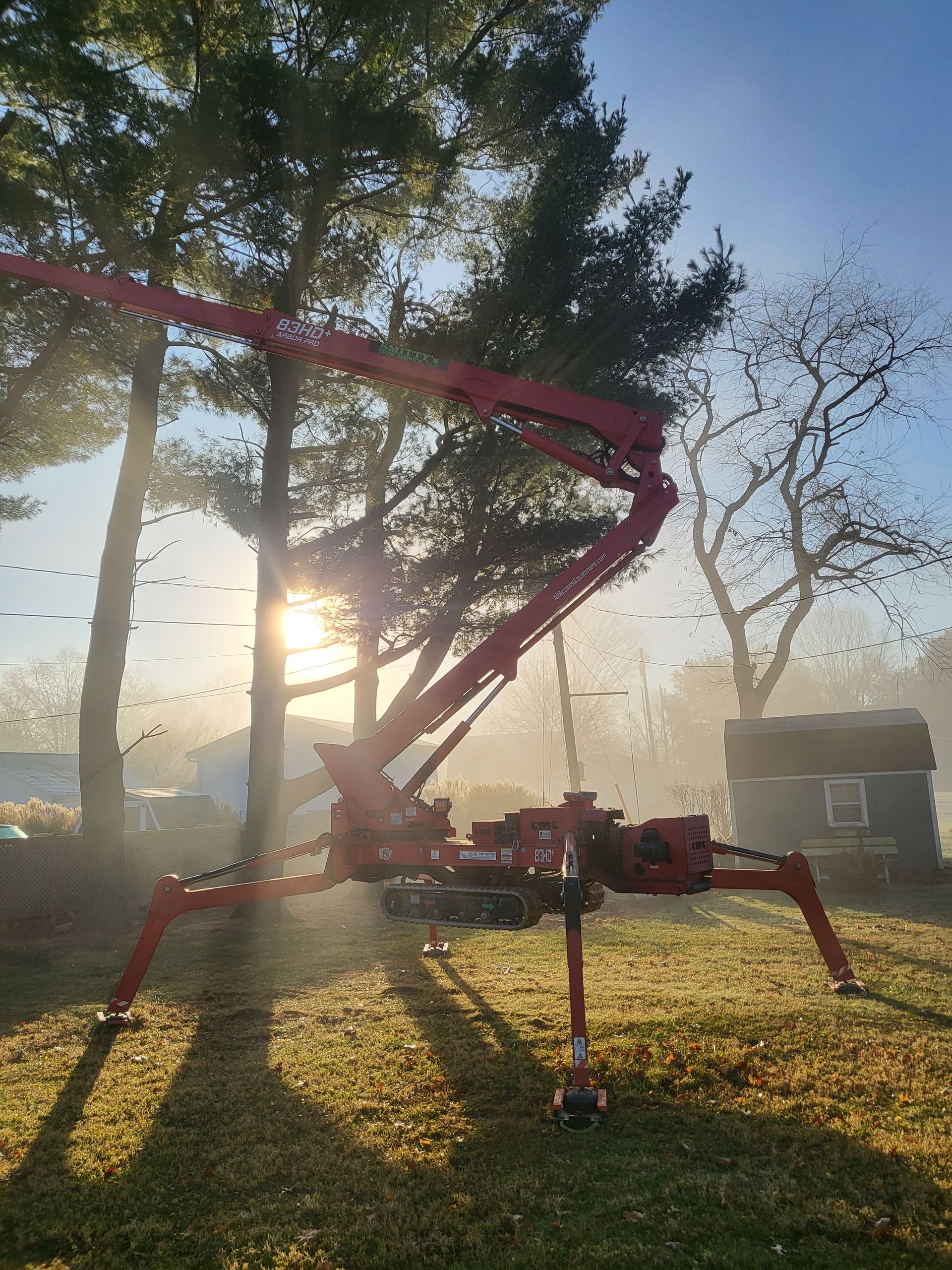 Red spider lift extended in a yard with trees and sunlight.