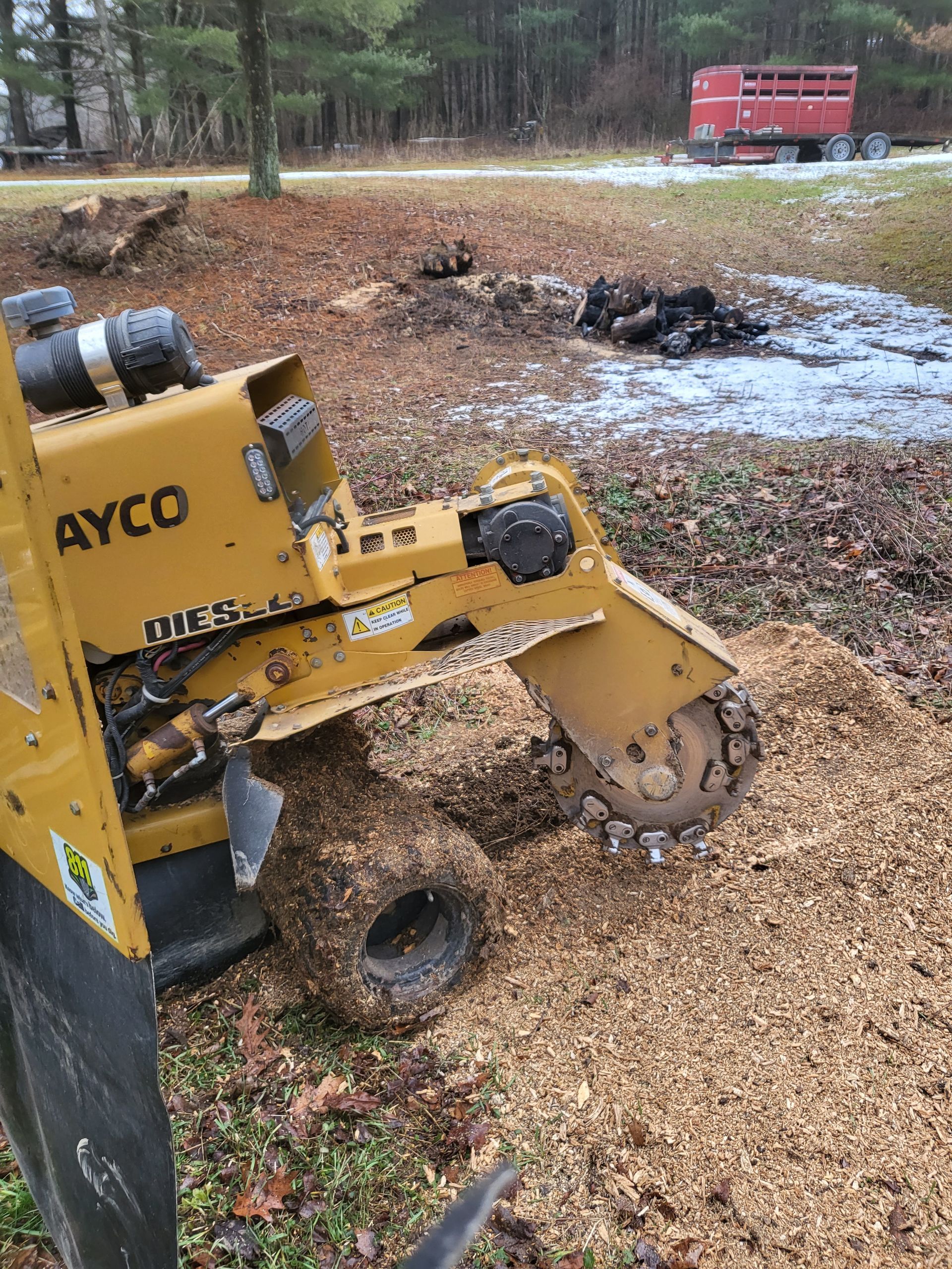 Yellow AYCO stump grinder at work, grinding a stump into wood chips. Outdoors.