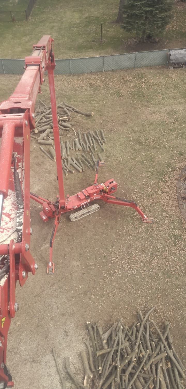 A red machine with an extending arm, on a brown surface with logs and wood chips.