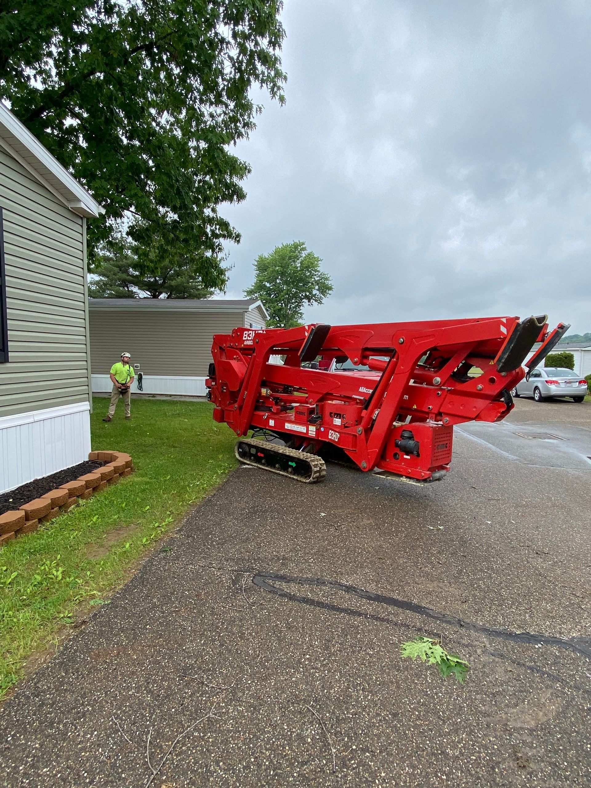 Red tracked machine parked on pavement next to a house; worker in the yard.