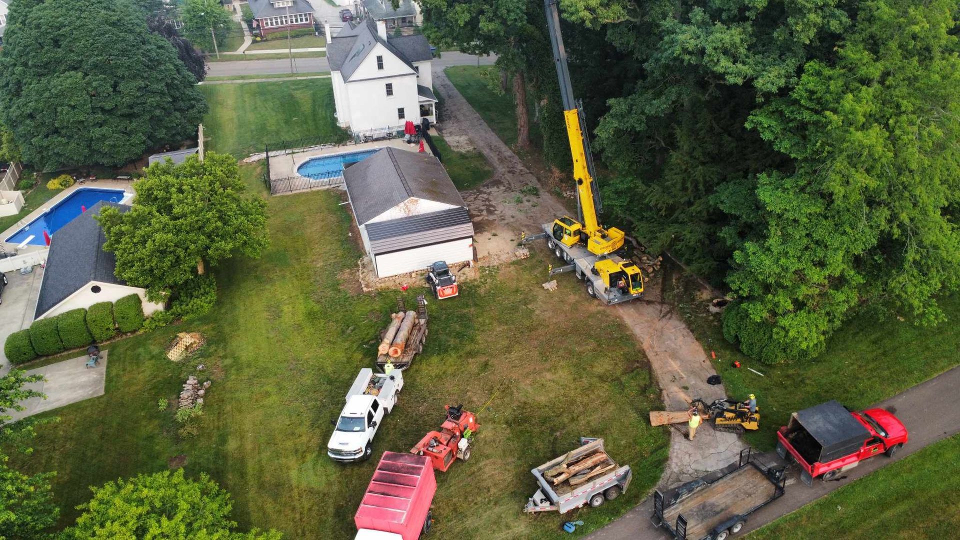 Aerial view of a crane removing a tree near a house and other vehicles in a residential area.