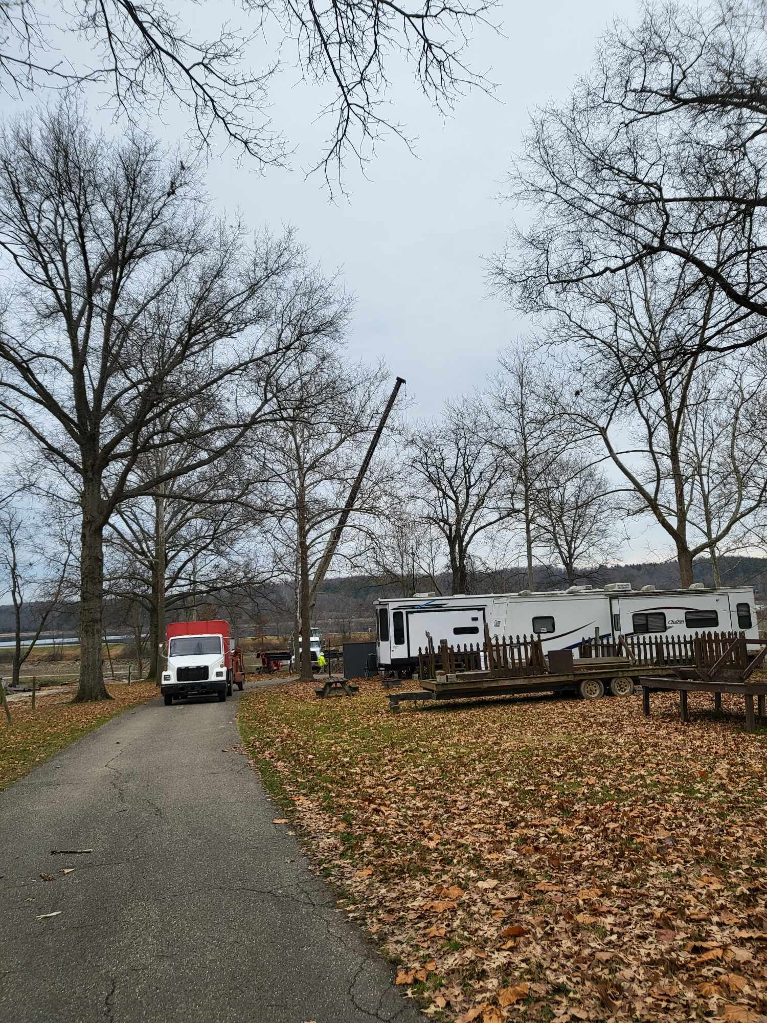 A work truck and crane near RVs in a park setting, autumn leaves on the ground.