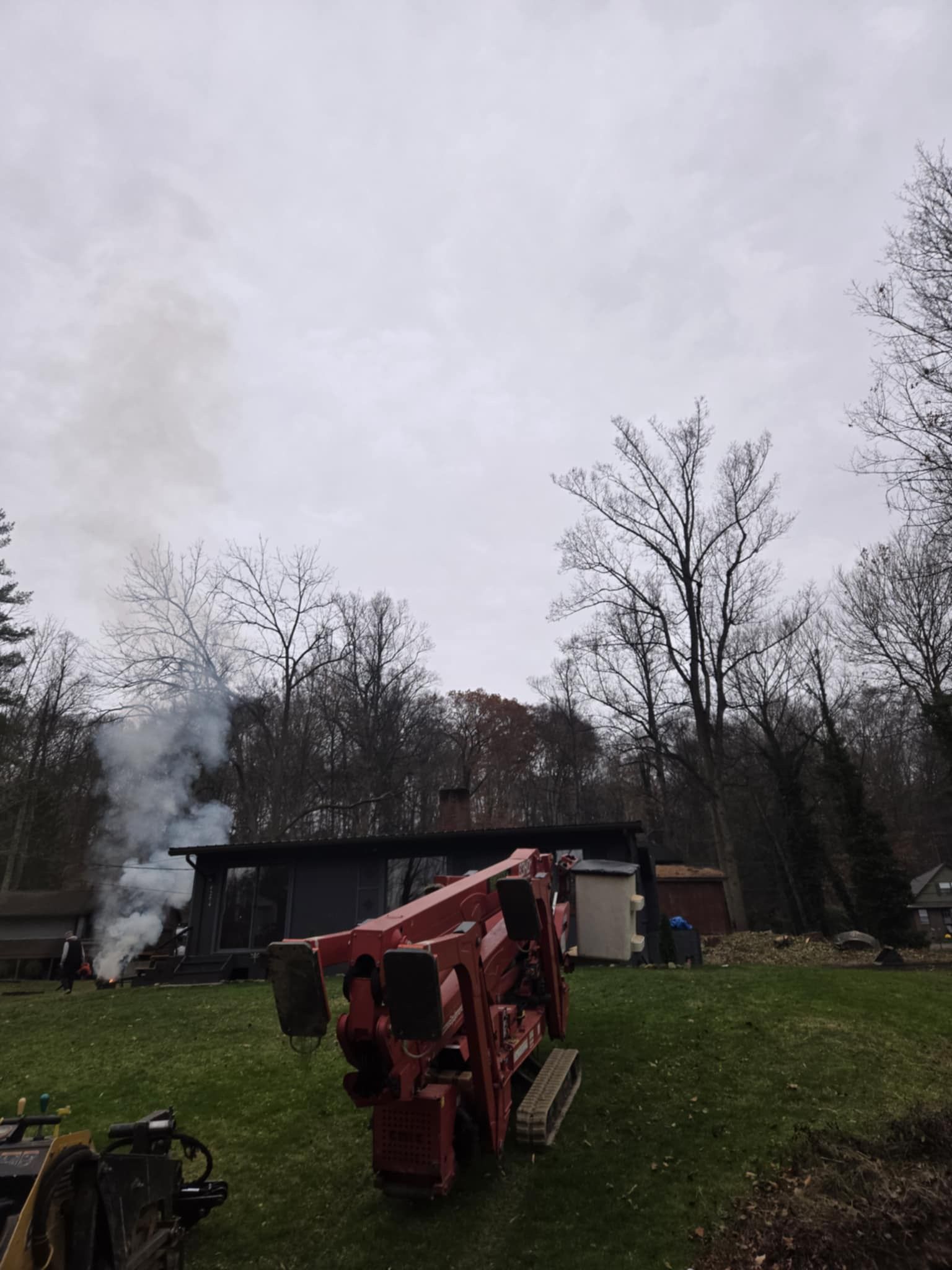 Smoke billows from a dark-roofed building. A red trencher sits on green grass. Trees in the background.