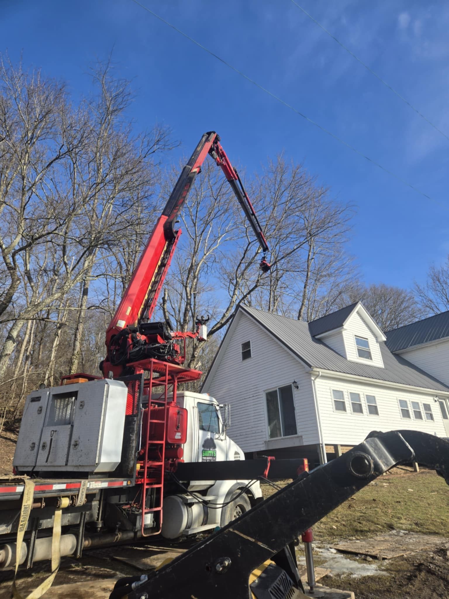 A red crane extends towards a white house, likely for construction. The setting is outdoors.