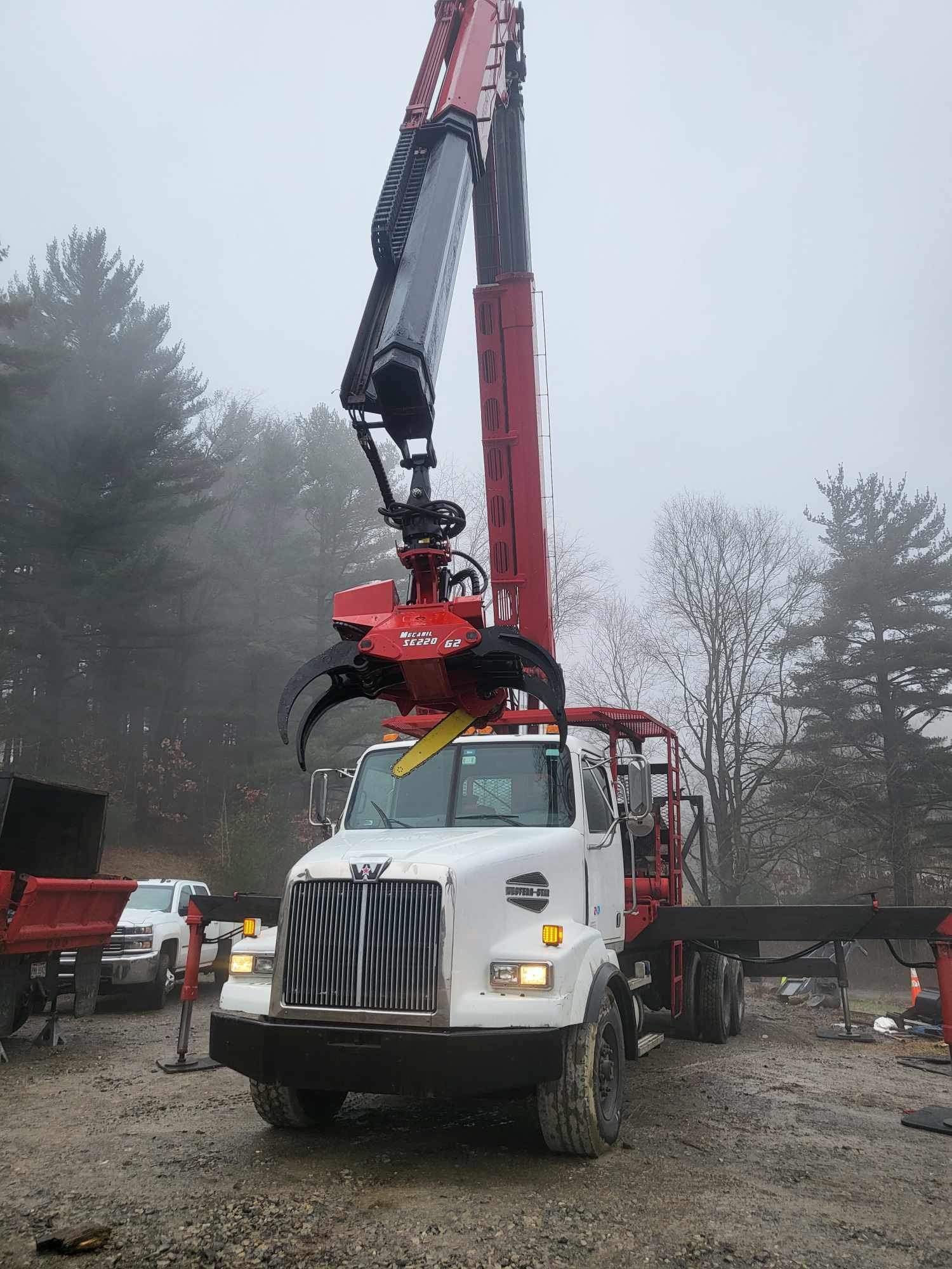 A red and white logging truck with a grapple arm, lifting logs in a foggy forest.