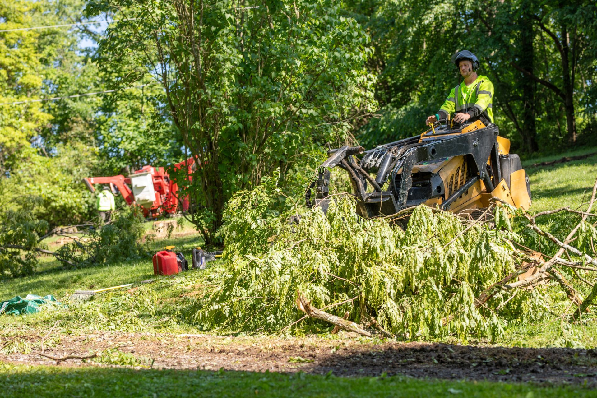 Man operating a stump grinder, removing tree branches on a grassy hill.