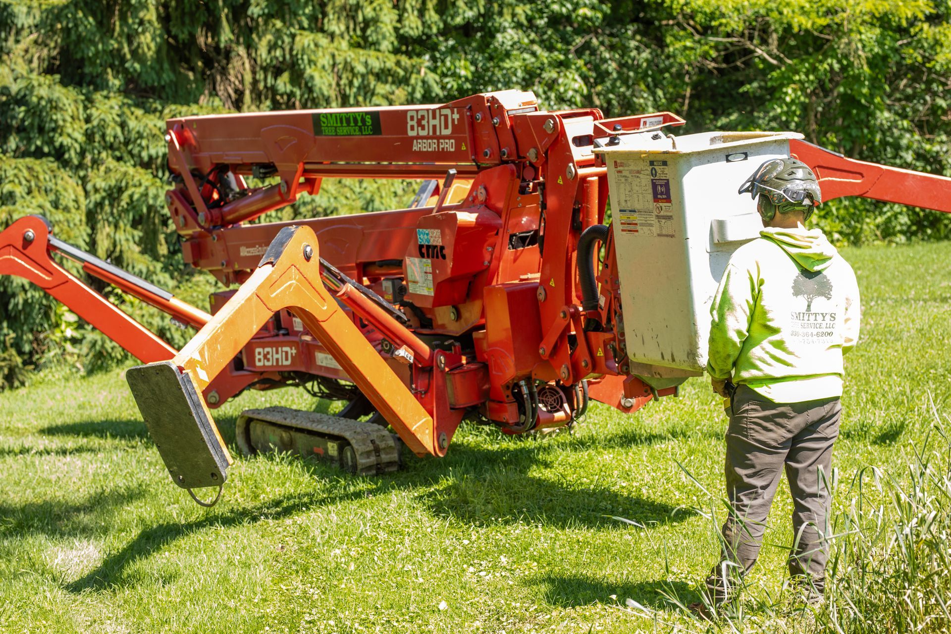 Red and orange tree service lift on tracks with worker in green clothing.