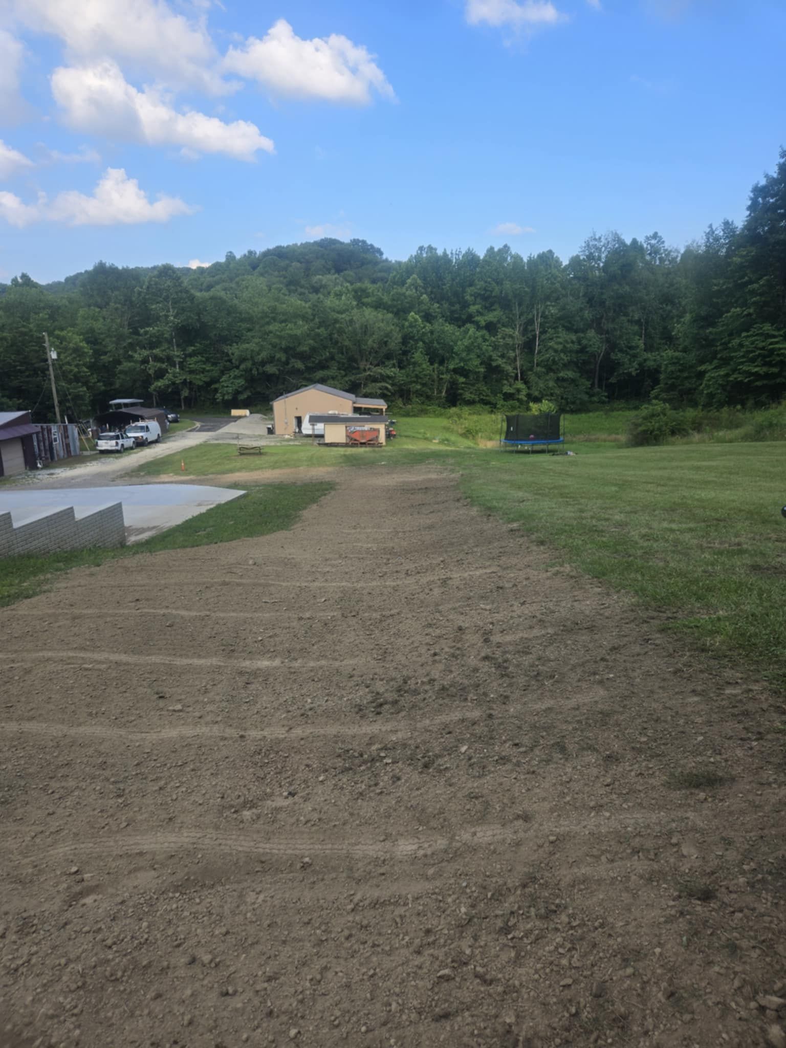 Dirt field with parallel lines, building, trees, and blue sky.