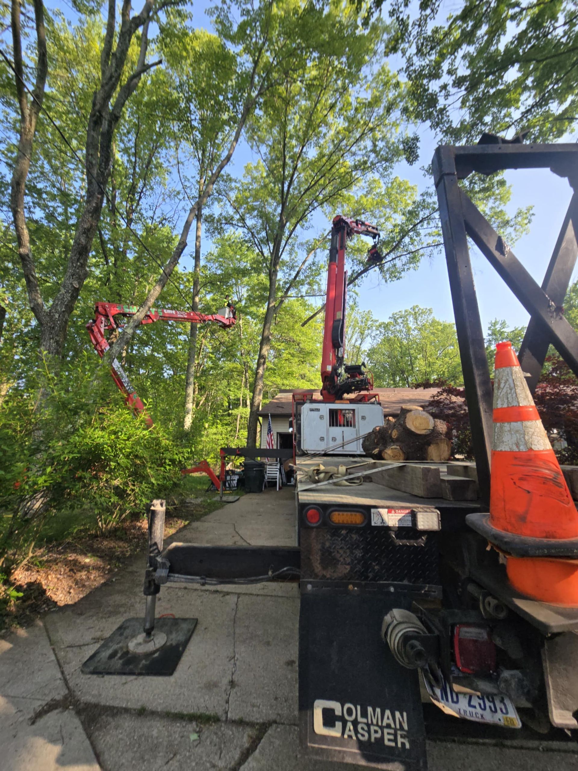 Tree service truck with lift arm extended, trimming trees near a house.