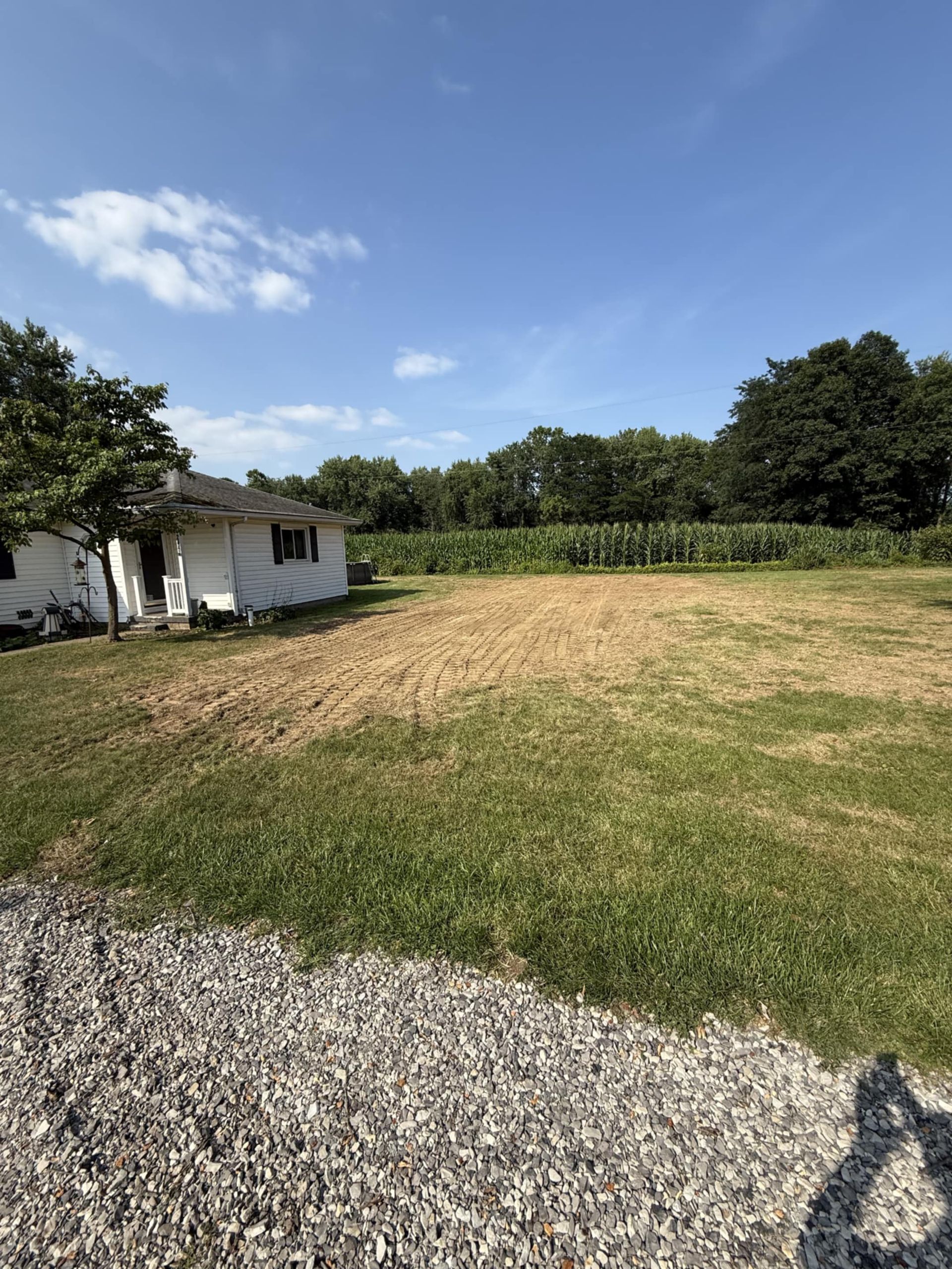 Small white building next to a field of cut hay and green grass under a blue sky.