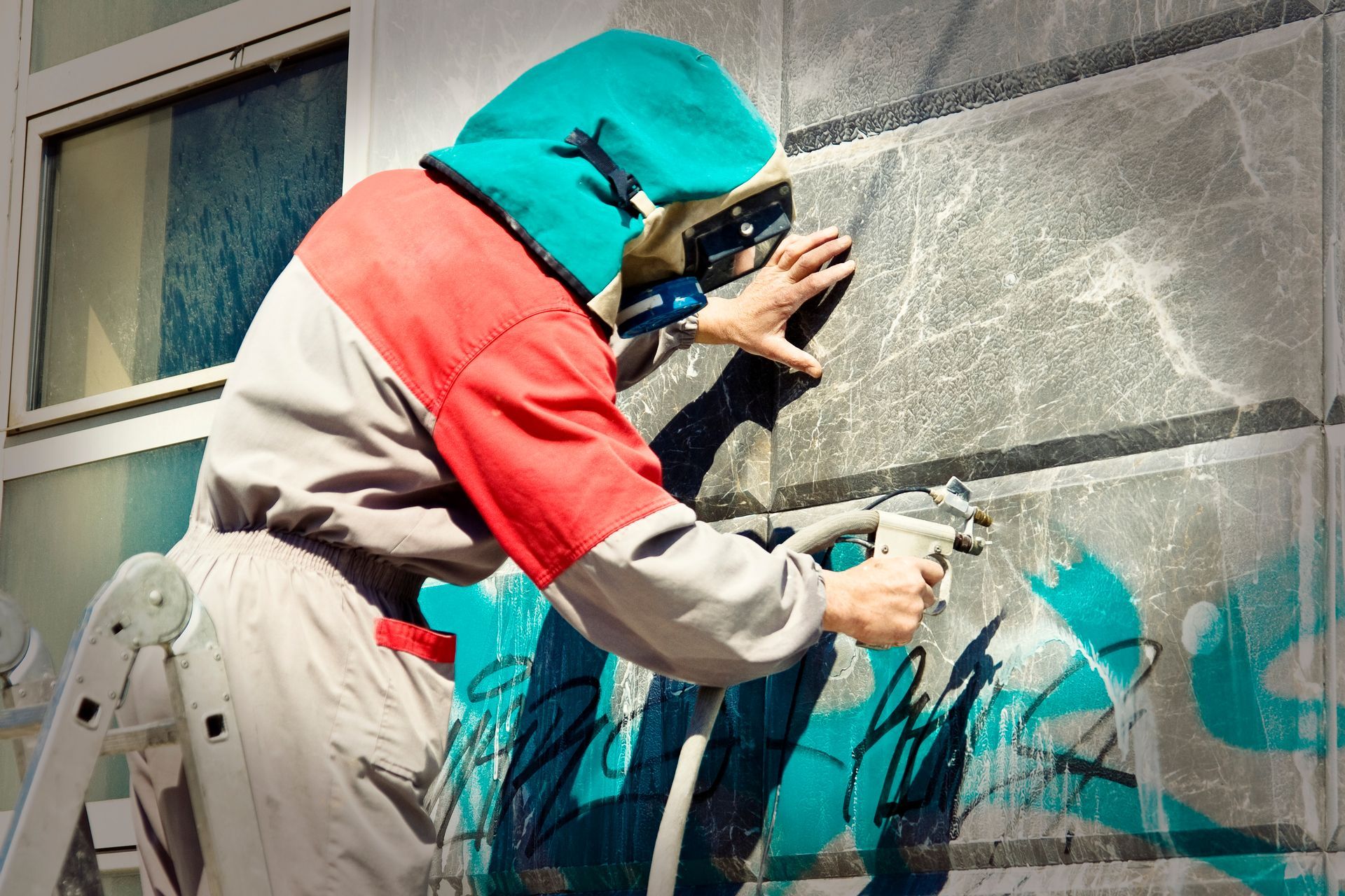 Person pressure-washing beige vinyl siding beside a white-trimmed window