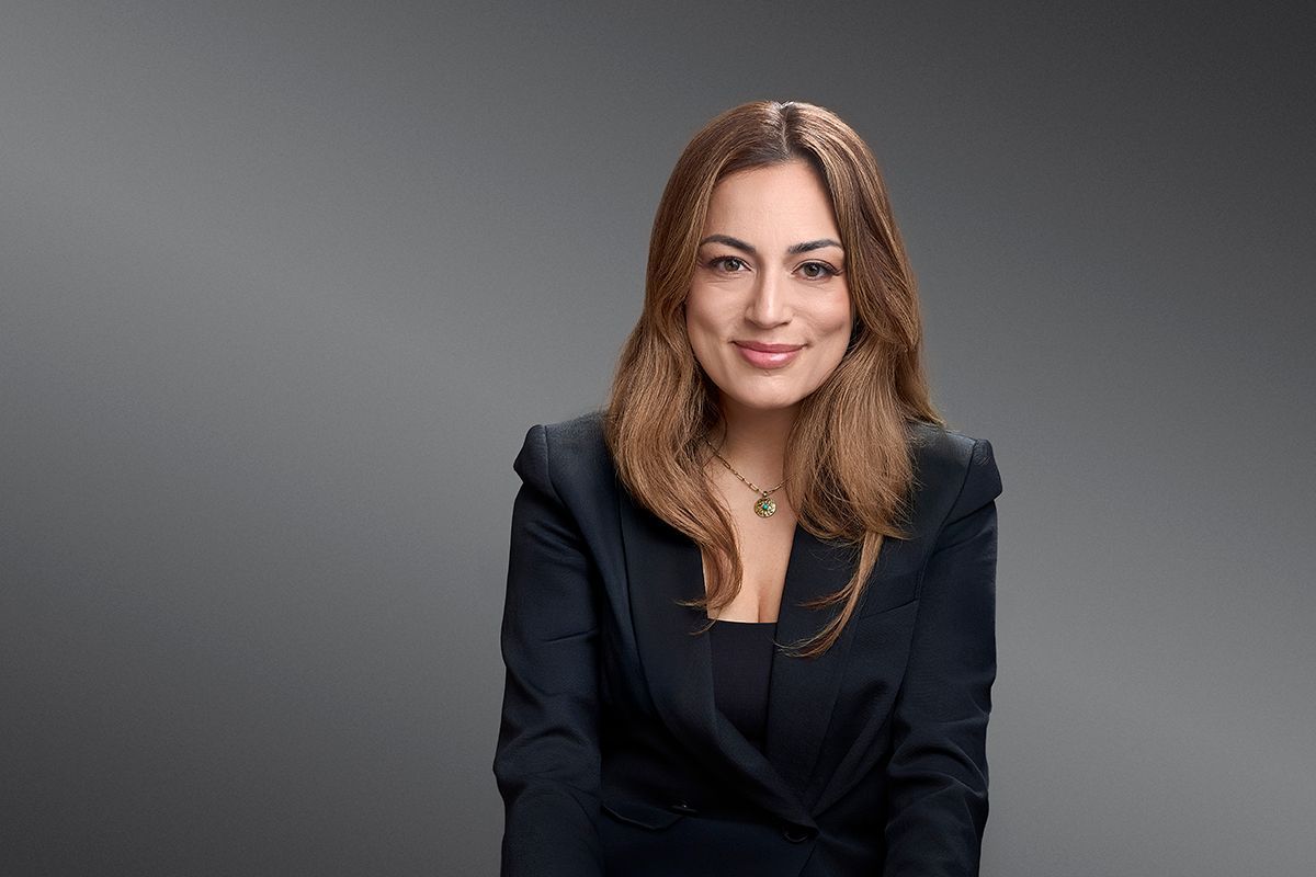 Jennifer Tsatsaronis is a smiling woman in a dark blazer posing against a grey background