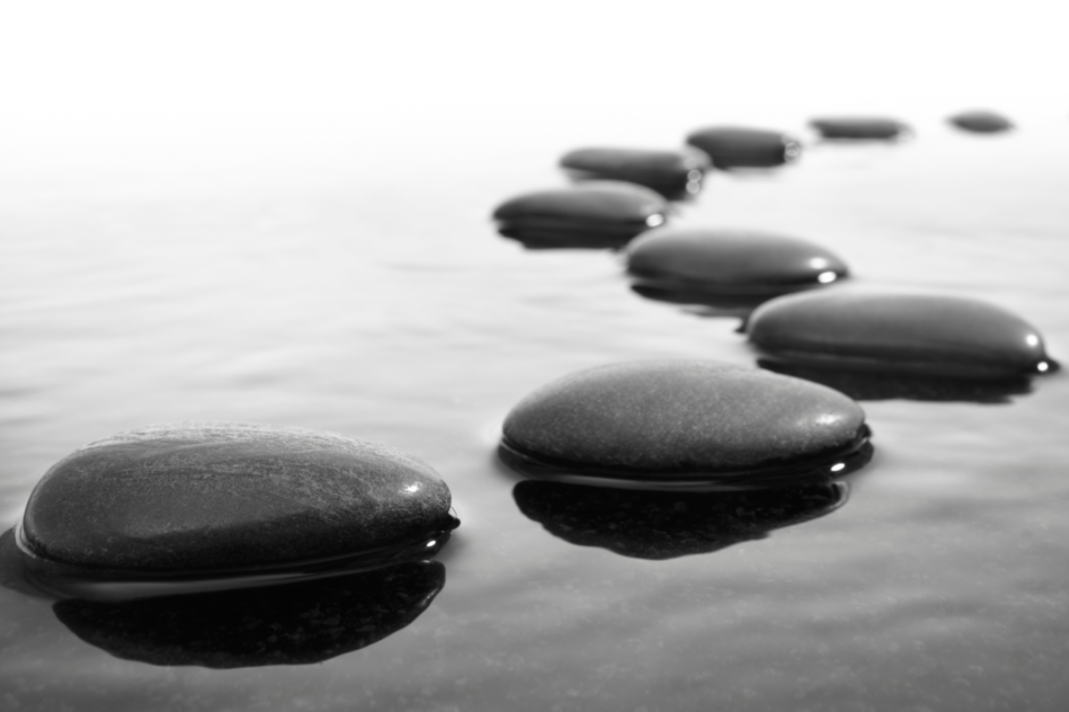 Black pebbles arranged in a winding line across calm water, with soft reflections about in-house counsel role