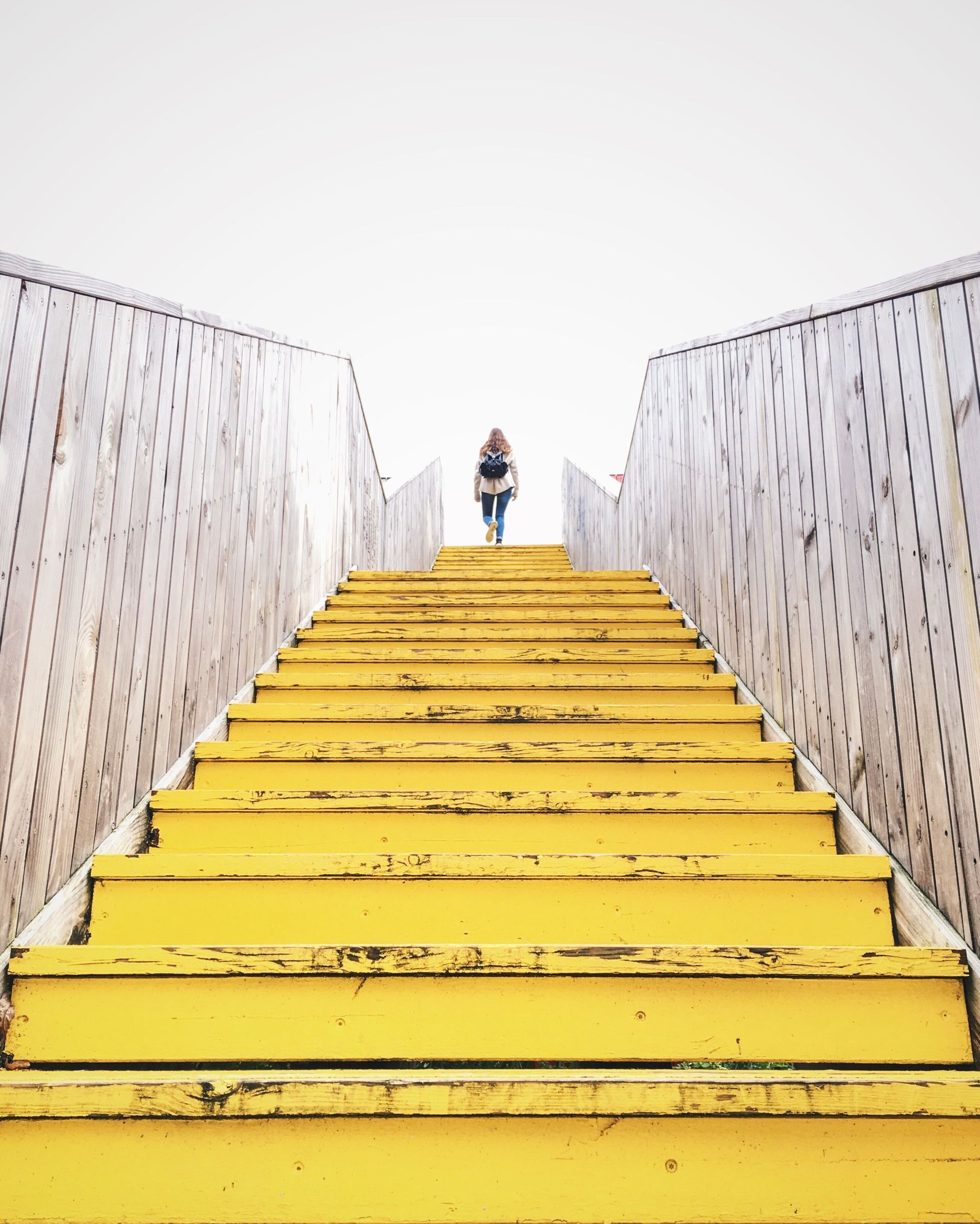 Yellow stairway with patterned side walls leading up to a small person at the top