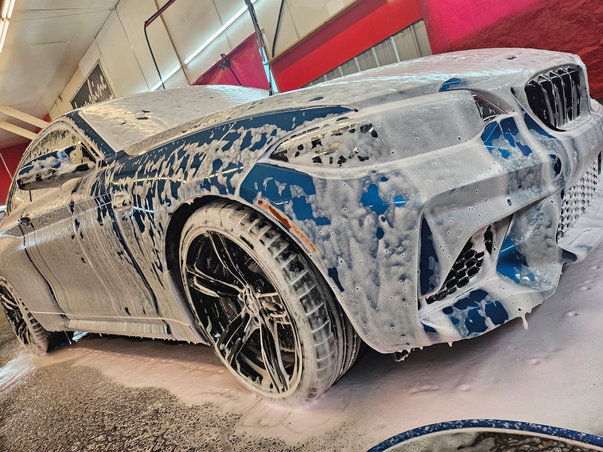 Blue and silver sports car covered in foam at a car wash.