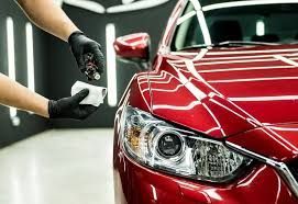 Person in black gloves applying ceramic coating to a red car's paint, indoor setting.