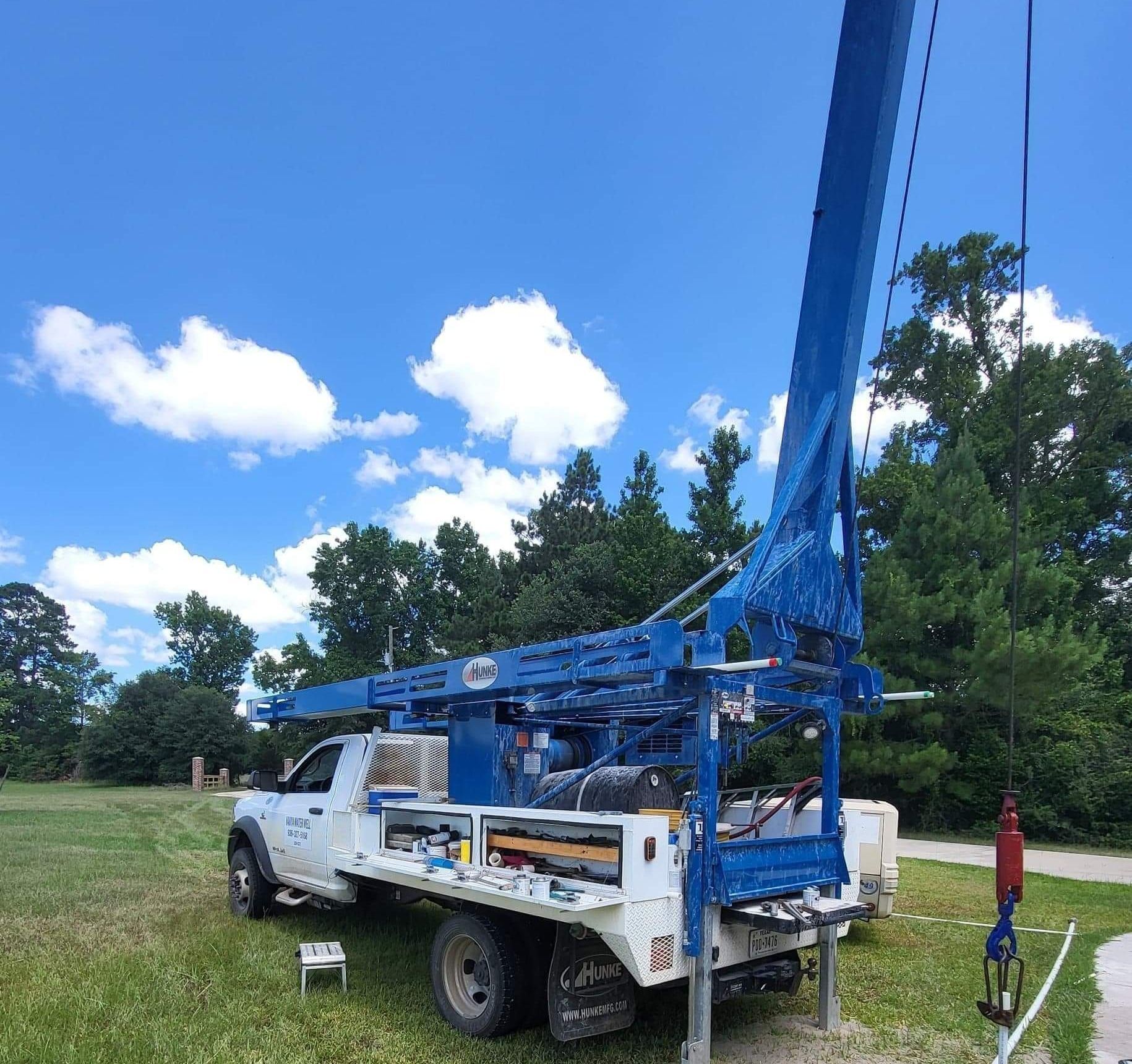 White utility truck with a tall blue boom lift parked on grass under a bright blue sky.