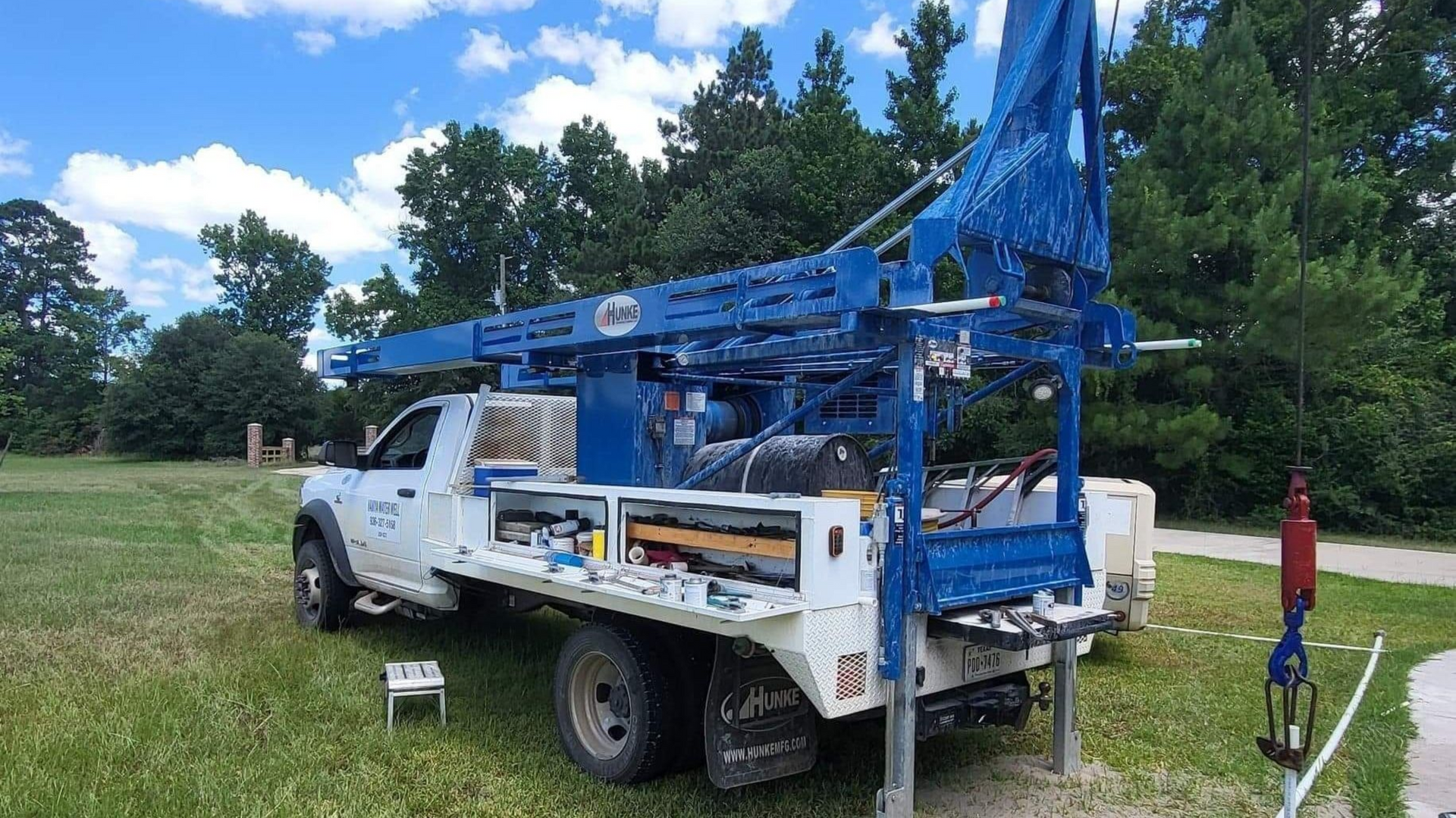 White utility truck with blue boom lift and open side compartments parked in a grassy field