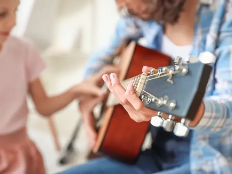 Image of a teacher showing a student how to use the guitar.
