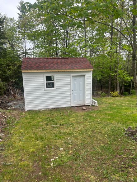 Small white shed with a red roof in a grassy yard, surrounded by trees.