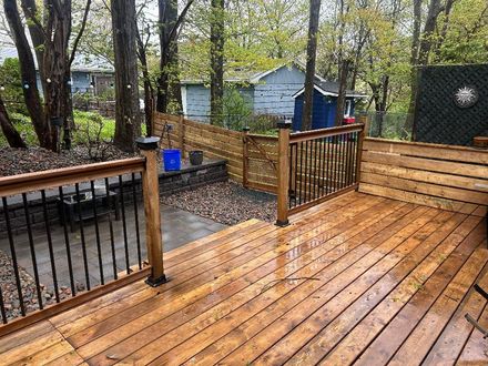 Rainy wooden deck with railing, picnic table, and blue sheds in a wooded backyard