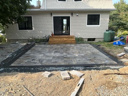 New stone patio and wooden steps leading to a house entry, with gravel and construction materials in front