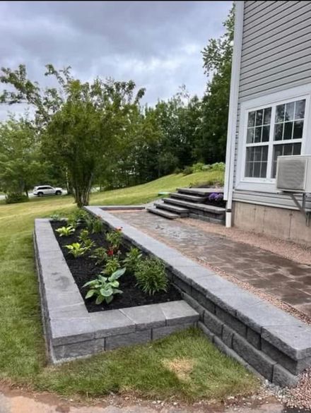 Raised garden bed beside house with gray stone edging, steps, and young plants in a yard