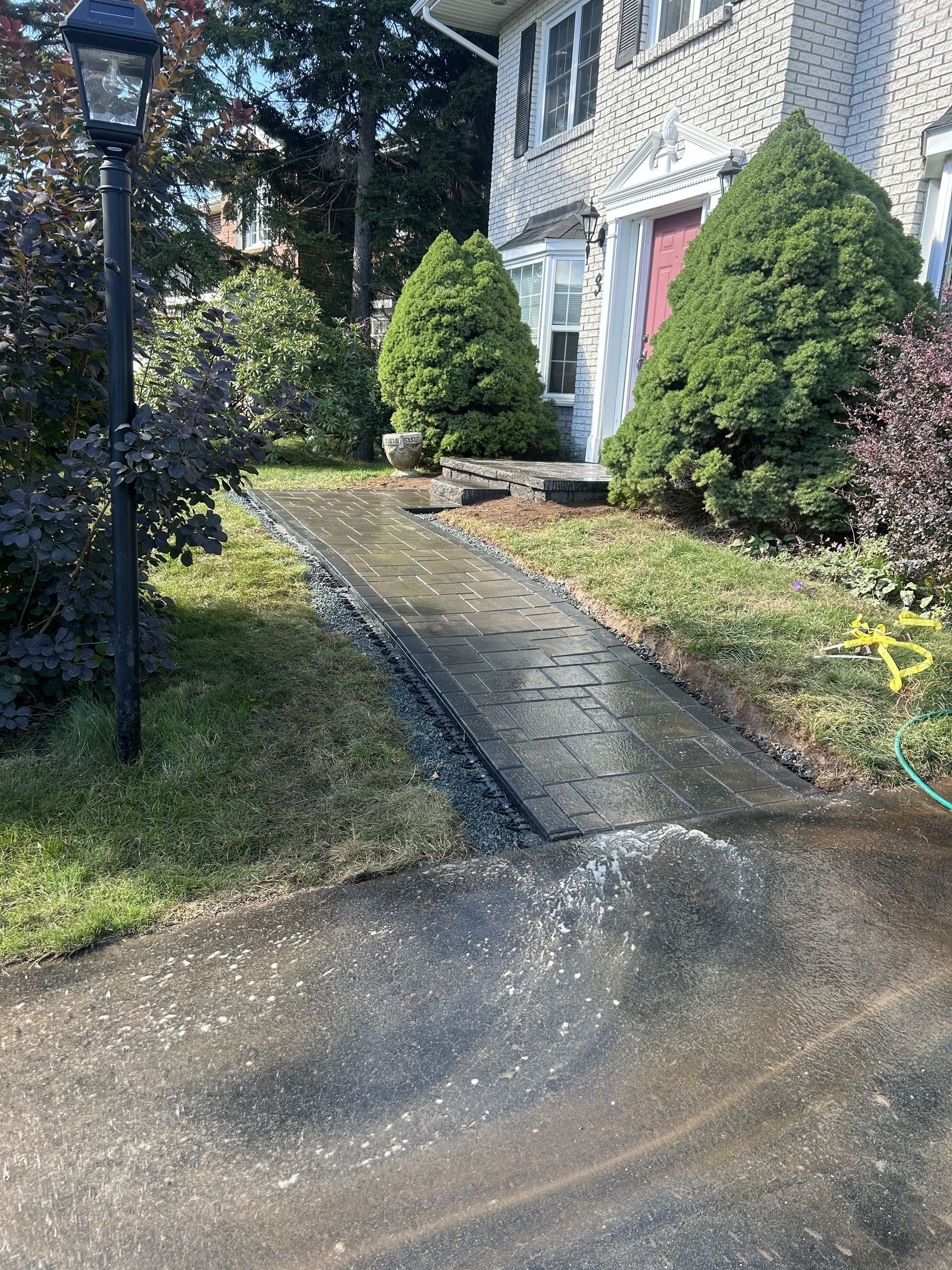 Stone walkway leading to a house entrance, bordered by trimmed shrubs and a black lamp post