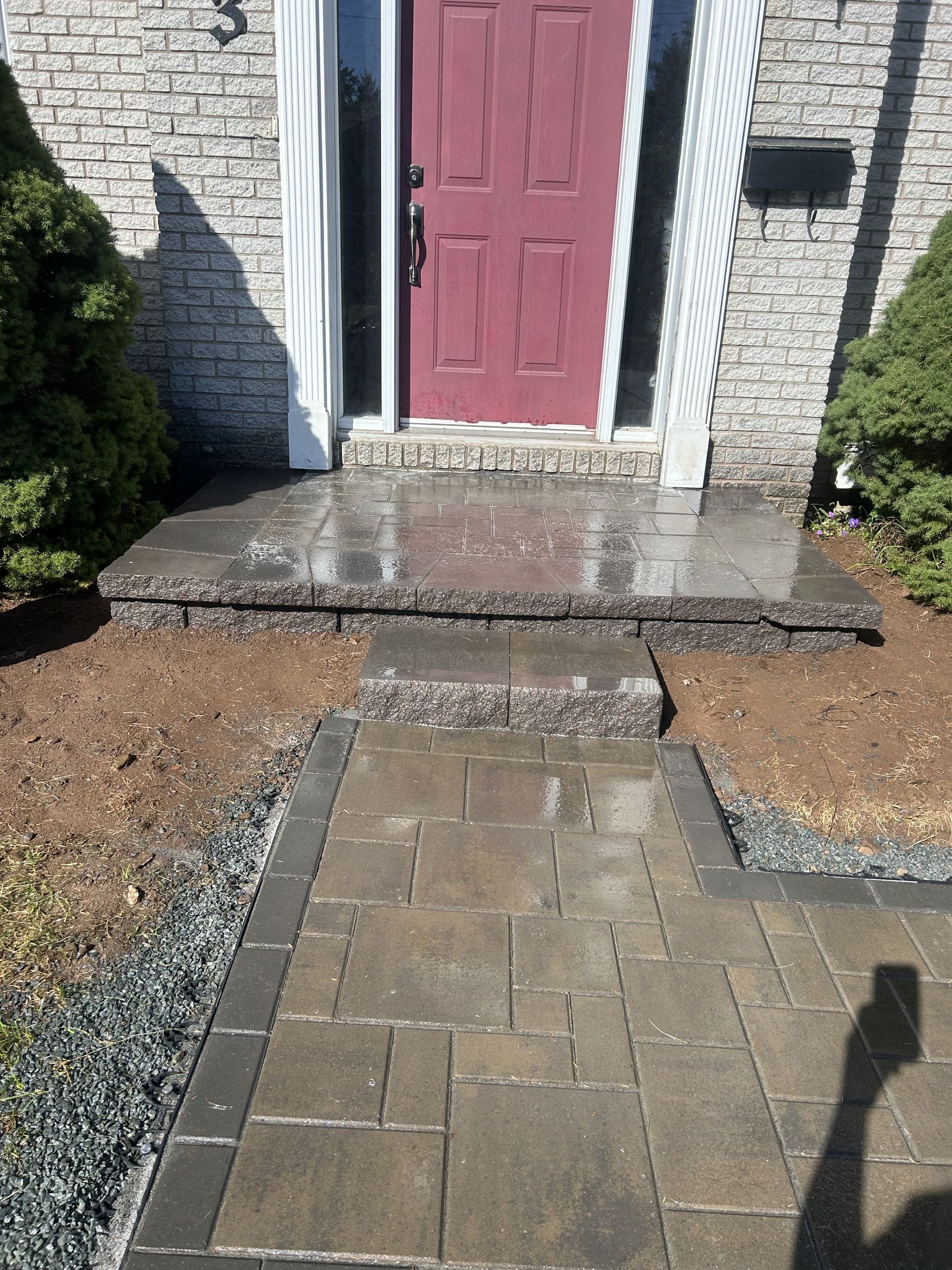 Front door with red door, stone steps, and a paved walkway leading up to a brick house