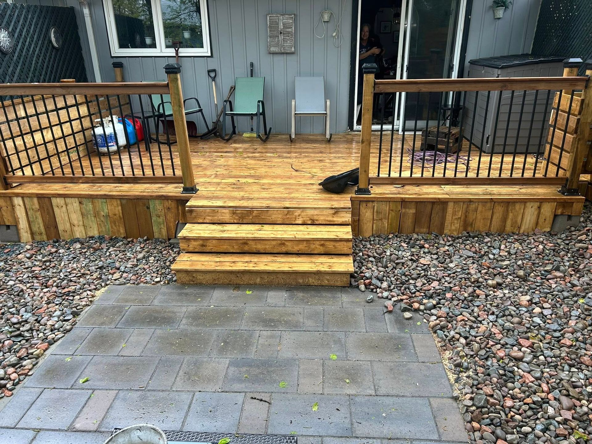 Wooden front porch with steps, black railings, and a gray paver walkway leading up to a house