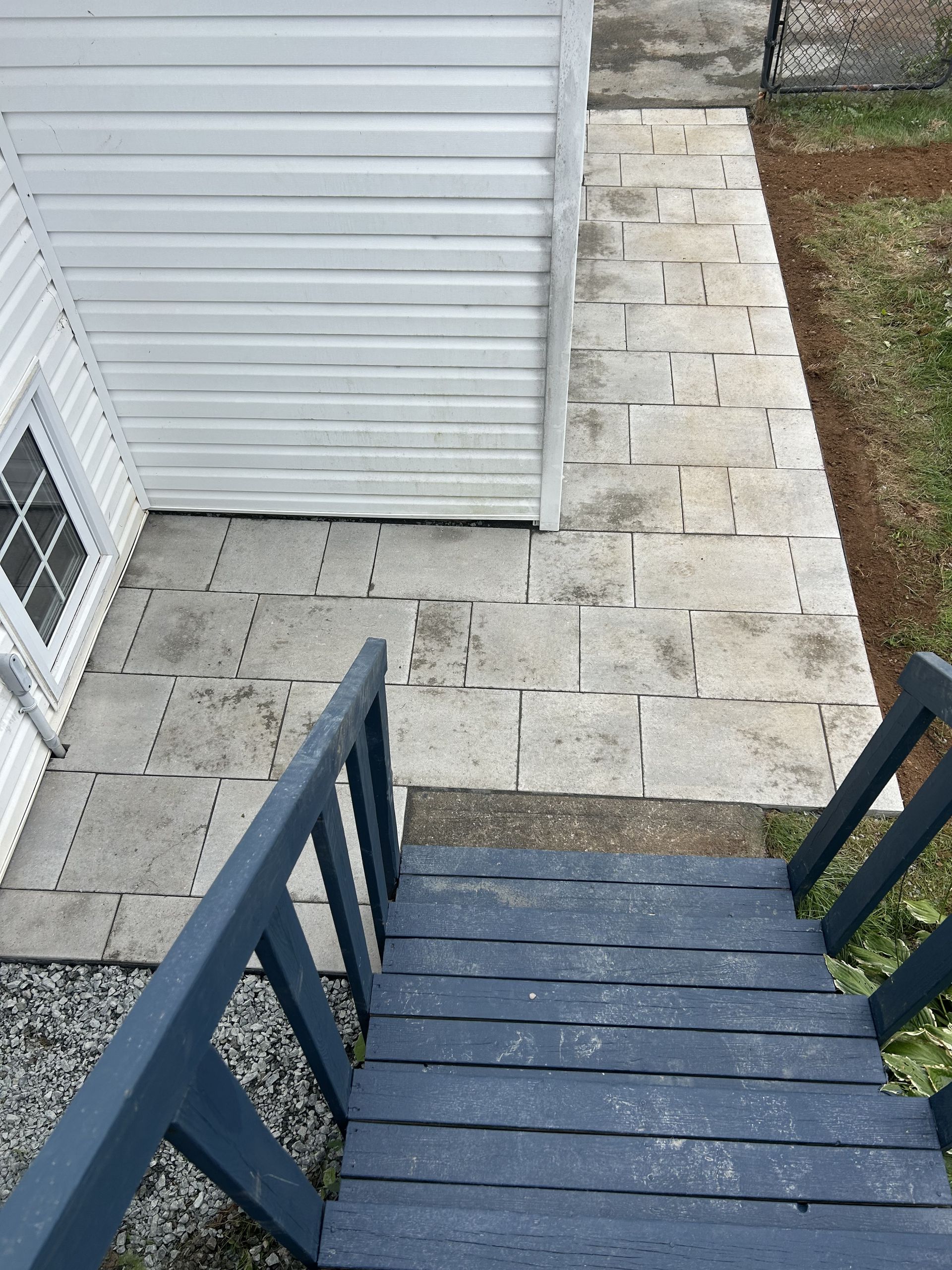 Blue-painted steps leading down to a stone patio beside a white-sided house