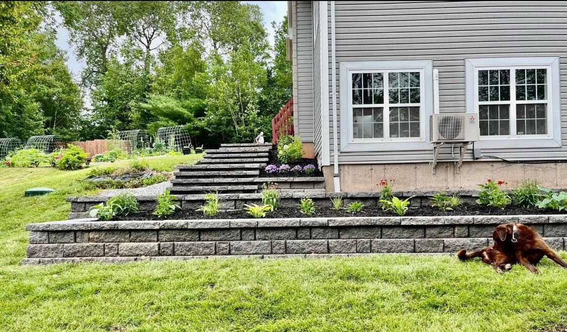 Stone terraced garden steps beside a gray house, with a dog lying on the lawn.