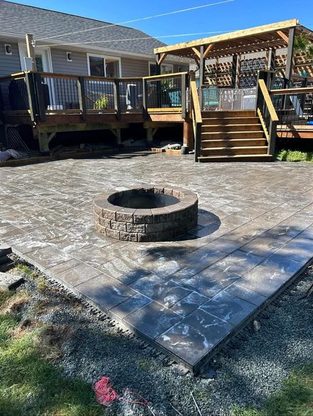 Backyard paver patio with stone fire pit, wooden deck, and stairs leading to a house