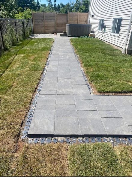 Backyard stone walkway leading to a wooden fence and patio area beside a house