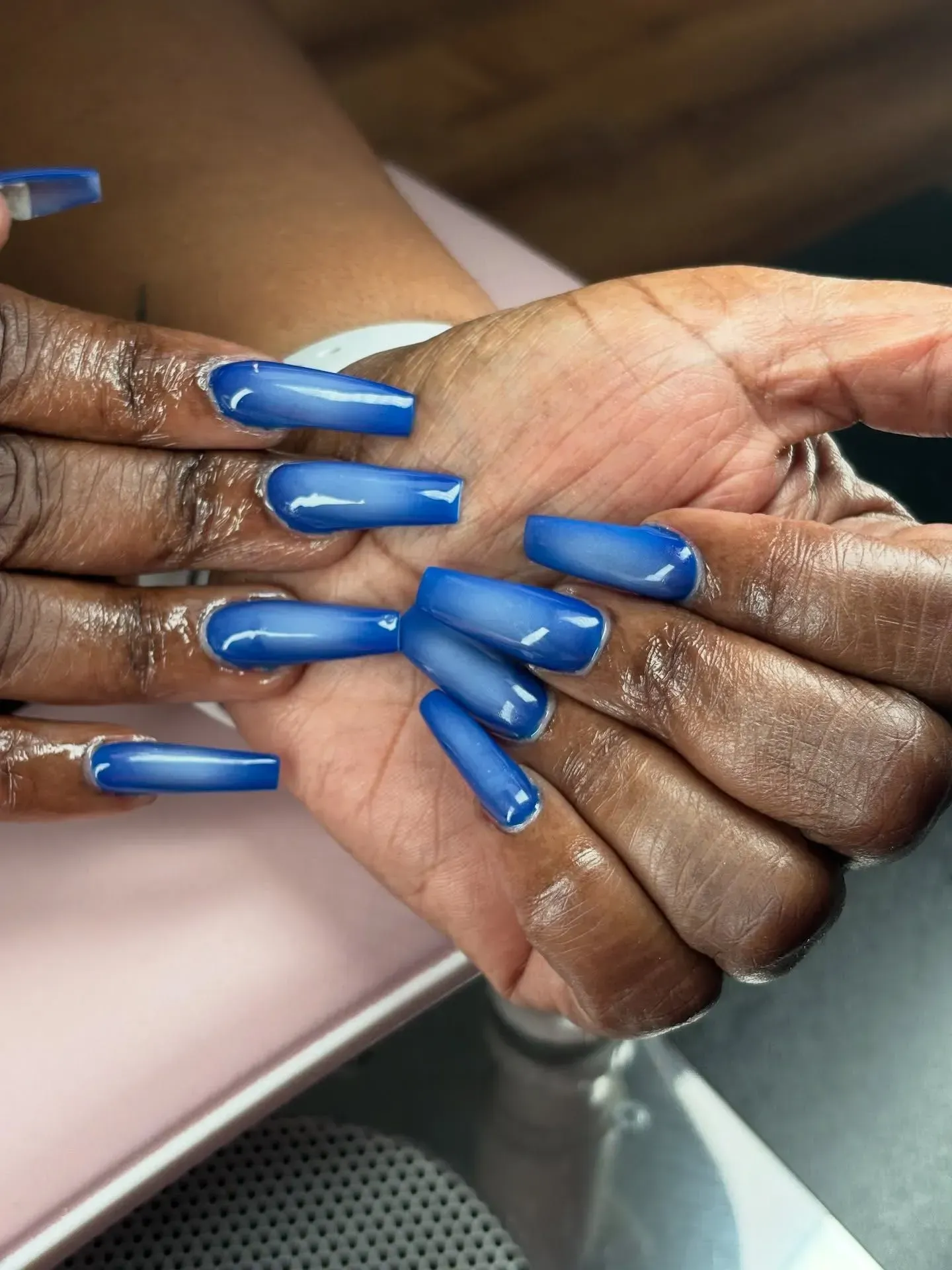 Hands with long blue acrylic nails clasped together over a table.