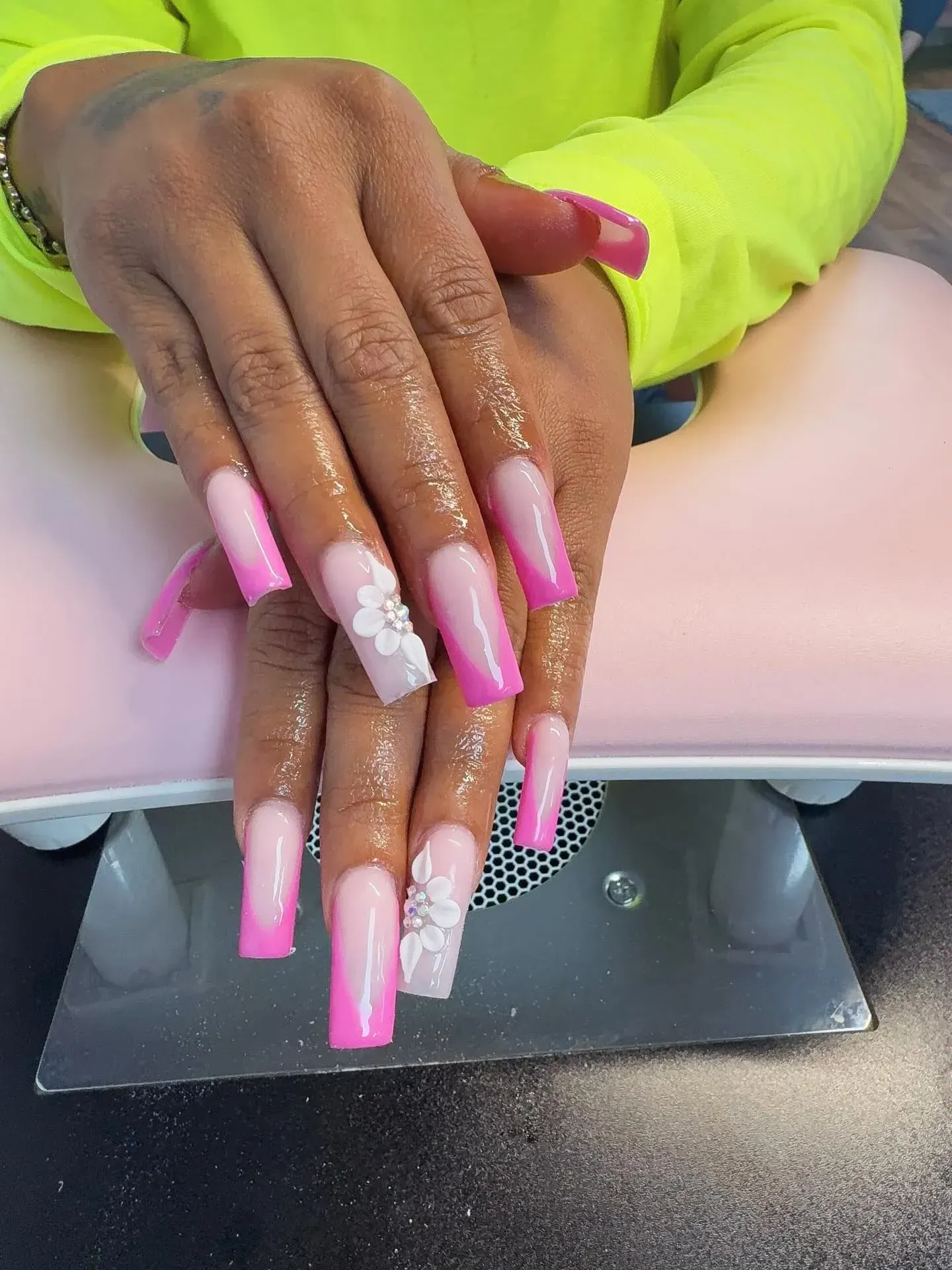 Hand with long pink and white decorated nails resting over a UV nail lamp at a manicure table