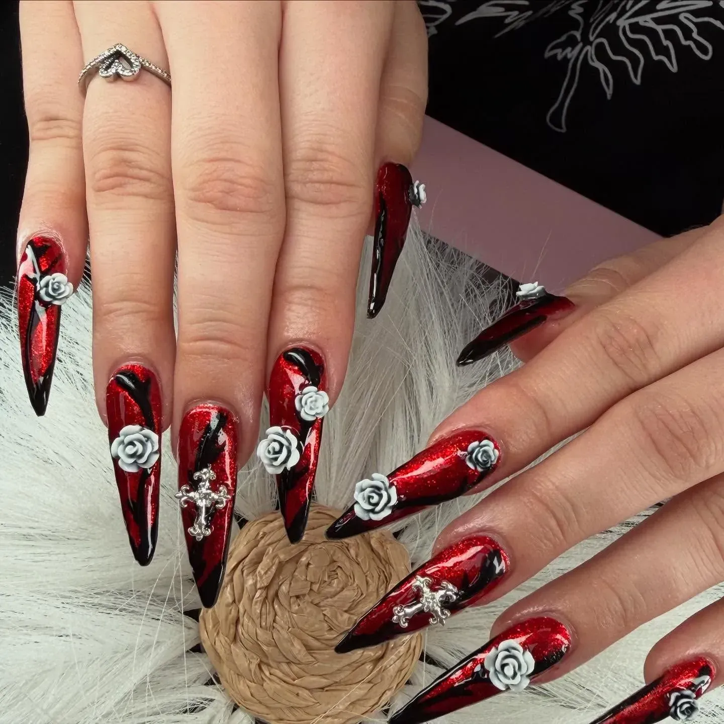 Hands with long red-and-black nail art and silver accents holding a rope knot.