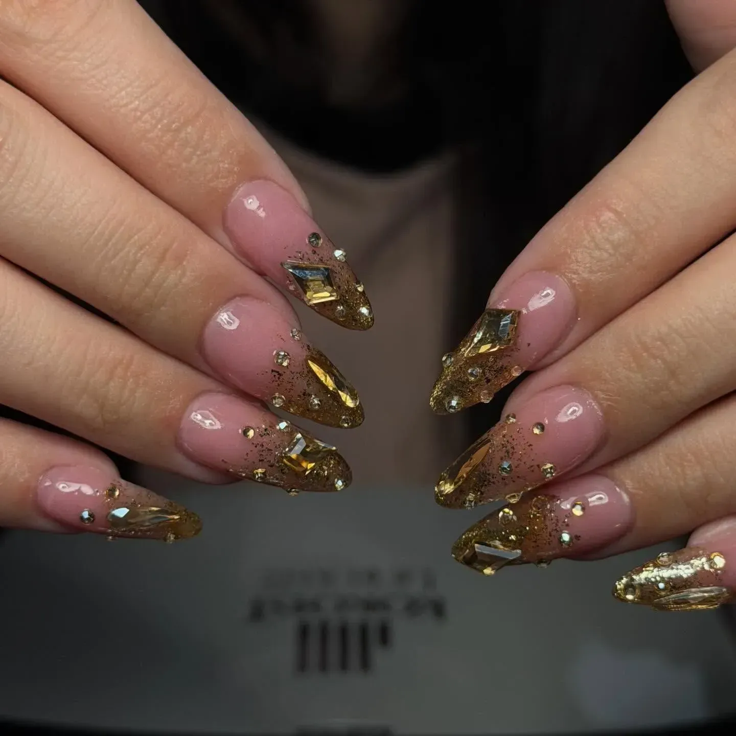 Hands with long pink-and-gold jeweled acrylic nails displayed over a nail salon table