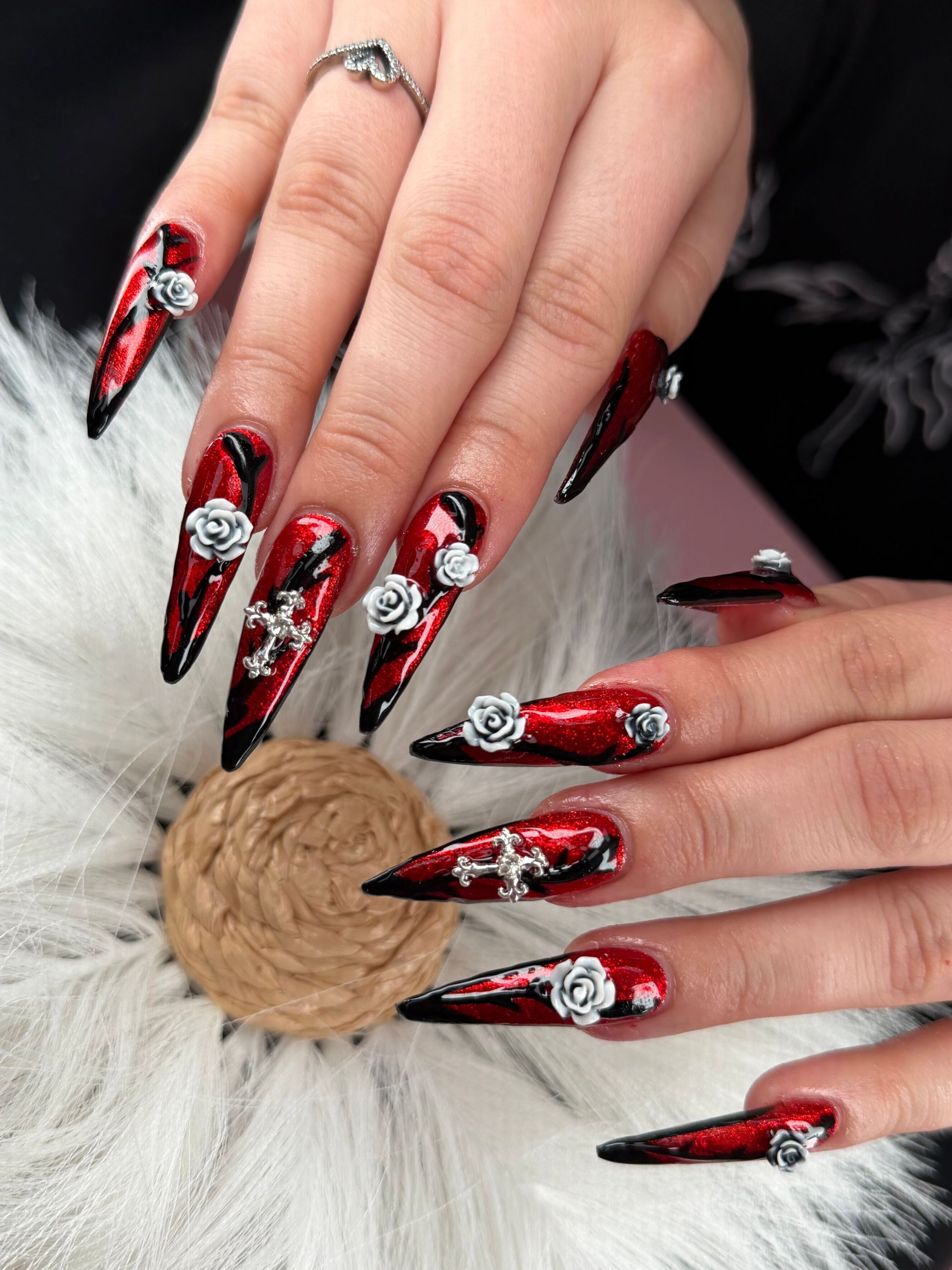 Long red-and-black stiletto nails with silver accents and rhinestones on hands over a white fur background