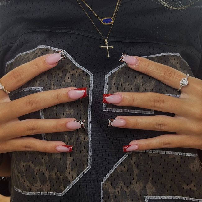 Hands with pink-red nails resting on a black lace top and layered necklaces.