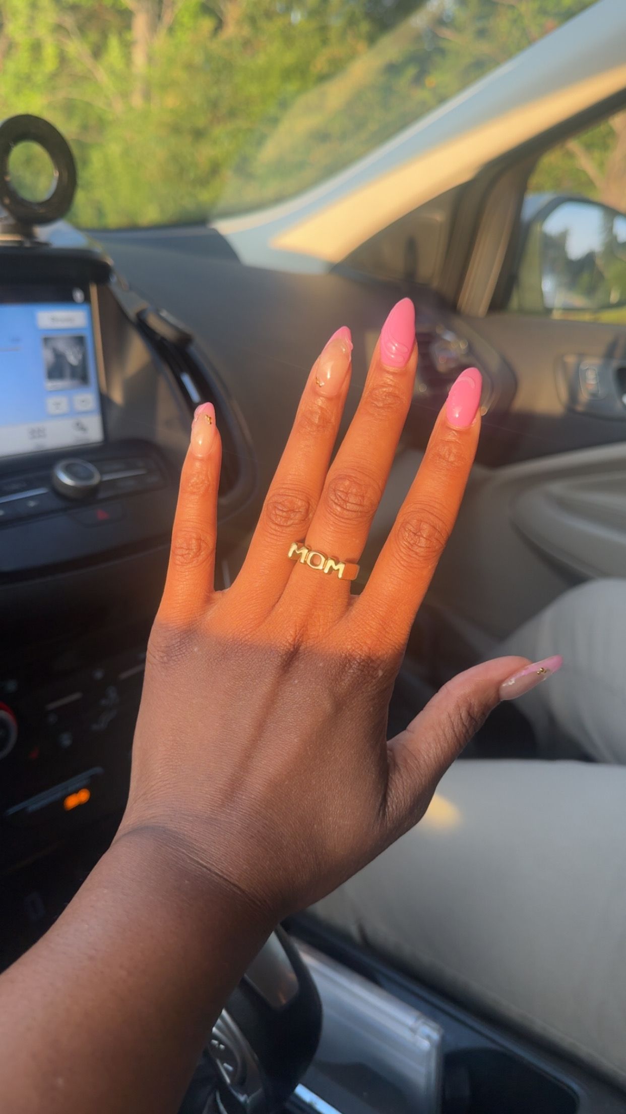Hand with long pink nails and gold ring resting inside a car, dashboard visible.