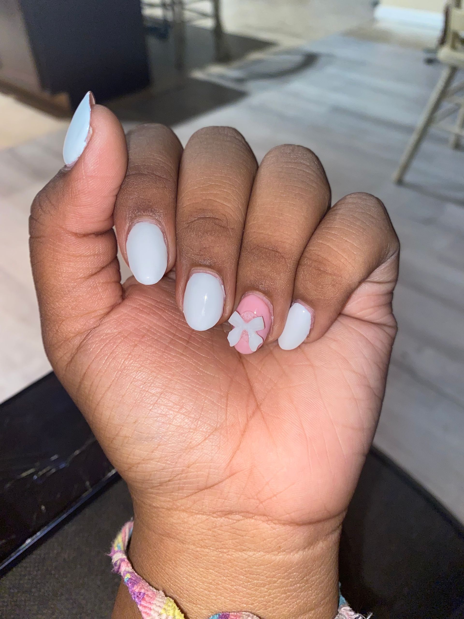Hand with white and pink manicured nails, including a pink floral accent nail, held up outdoors.