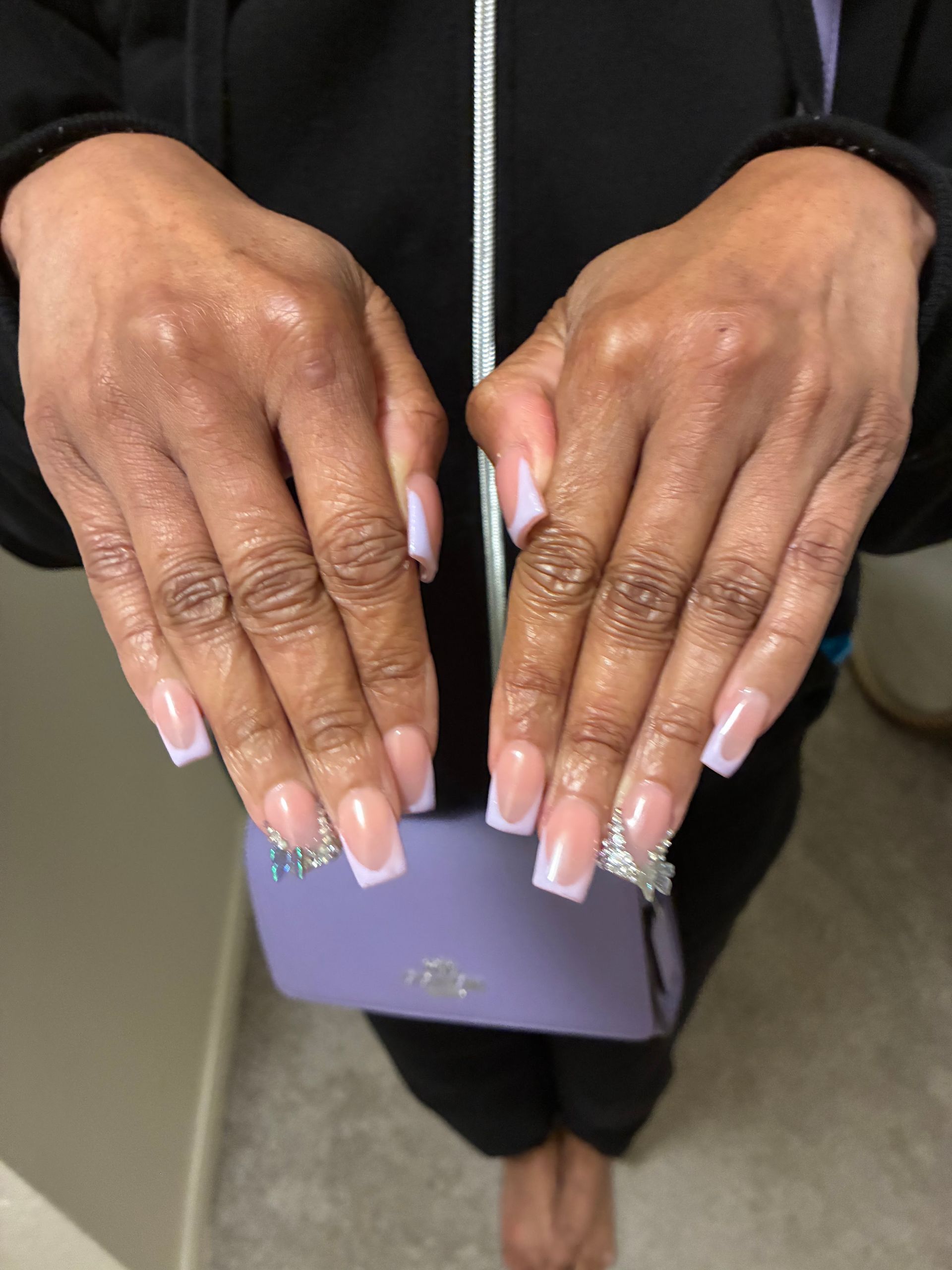 Hands with long pink-and-white nails holding a small lavender purse.