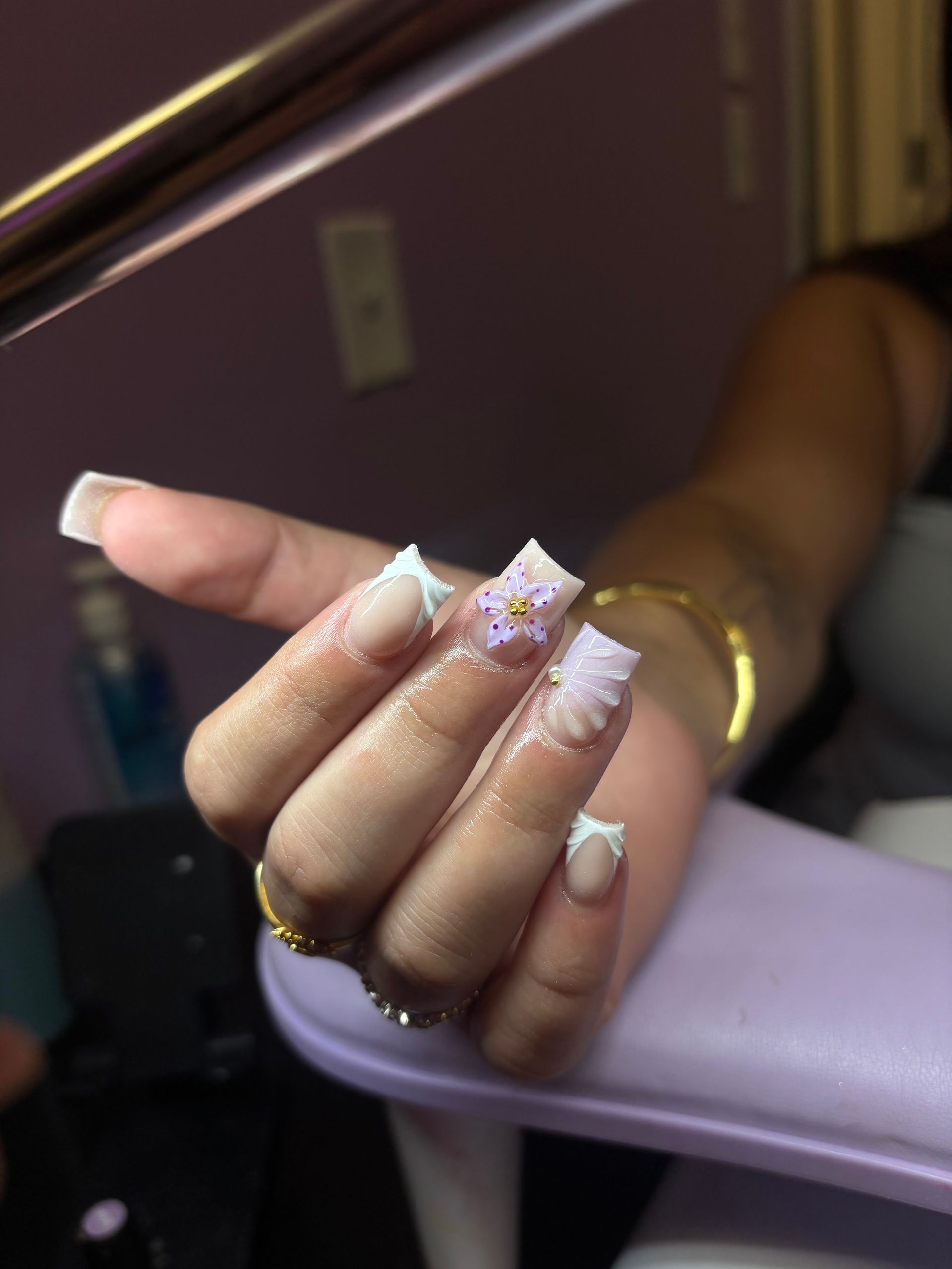 Hand with long lavender and white nails resting on a lilac armrest in a salon chair