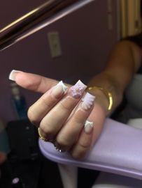 Hand with long white and gold acrylic nails resting on a lavender armrest.