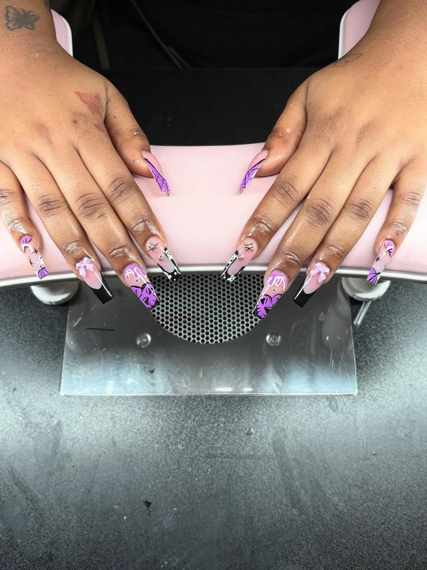Hands with long purple acrylic nails resting on a pink manicure hand rest.