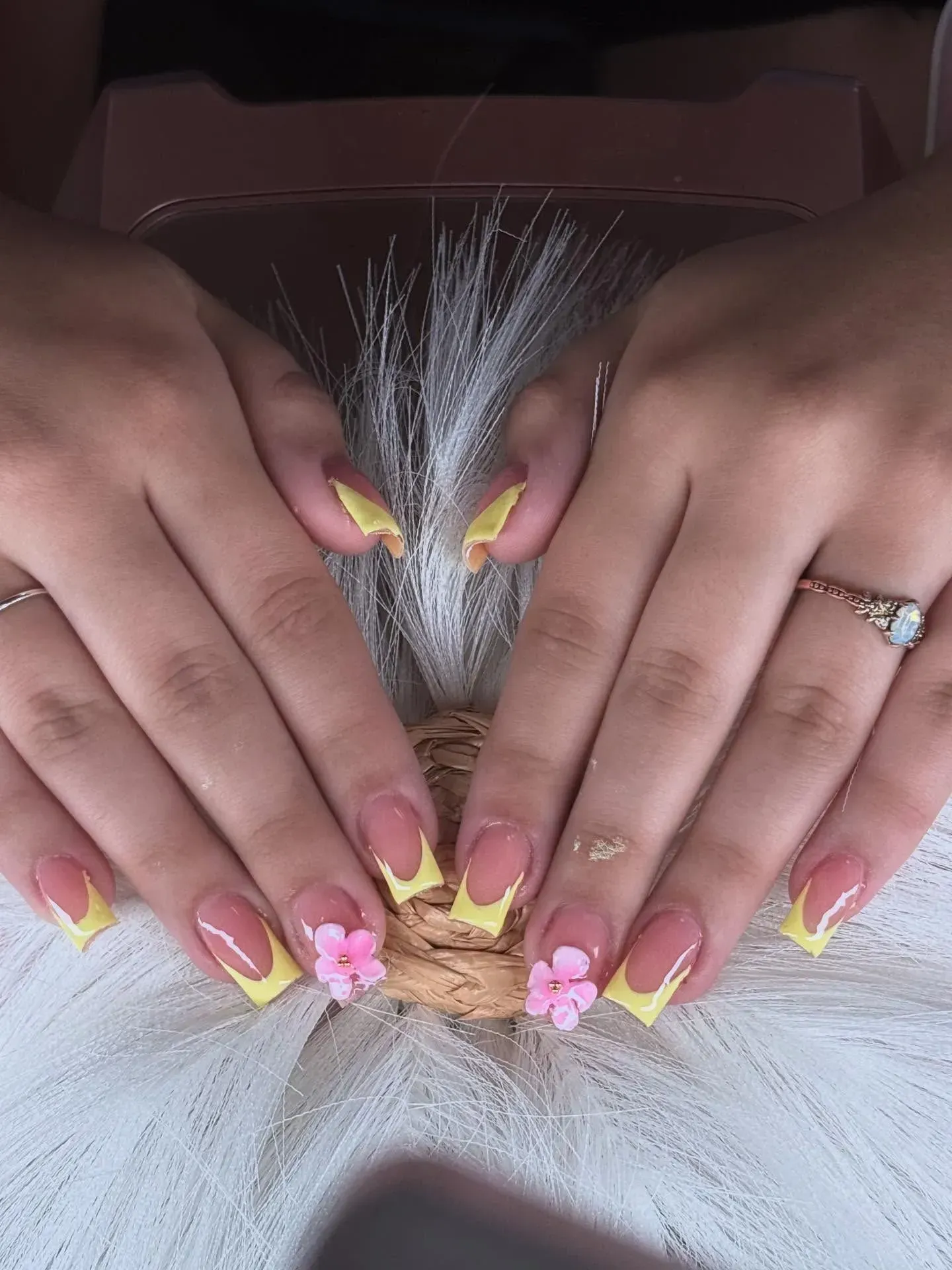 Hands with yellow and pink nails holding a white feathery bouquet or decorative fan.