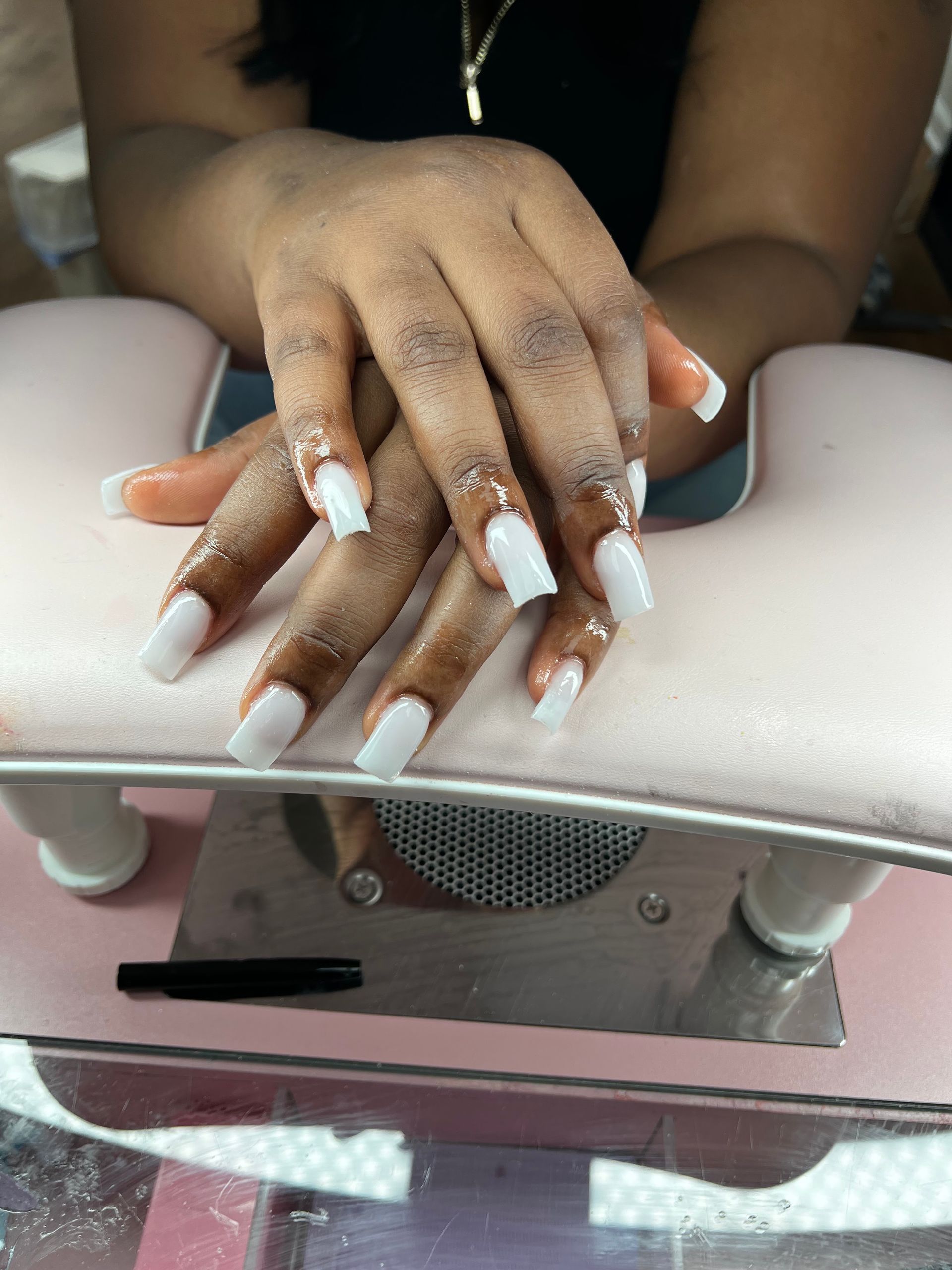 White acrylic nails resting on a pink manicure hand cushion at a nail salon