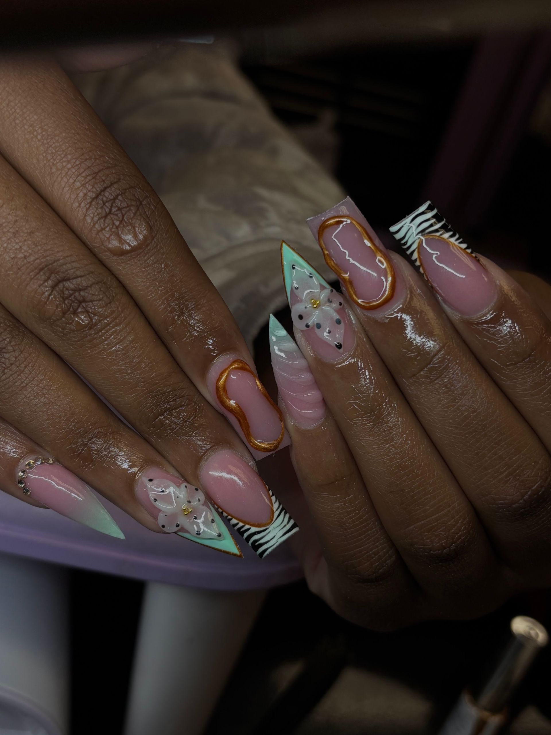 Hands with long pastel pink and mint nail art with gold accents and rhinestones.